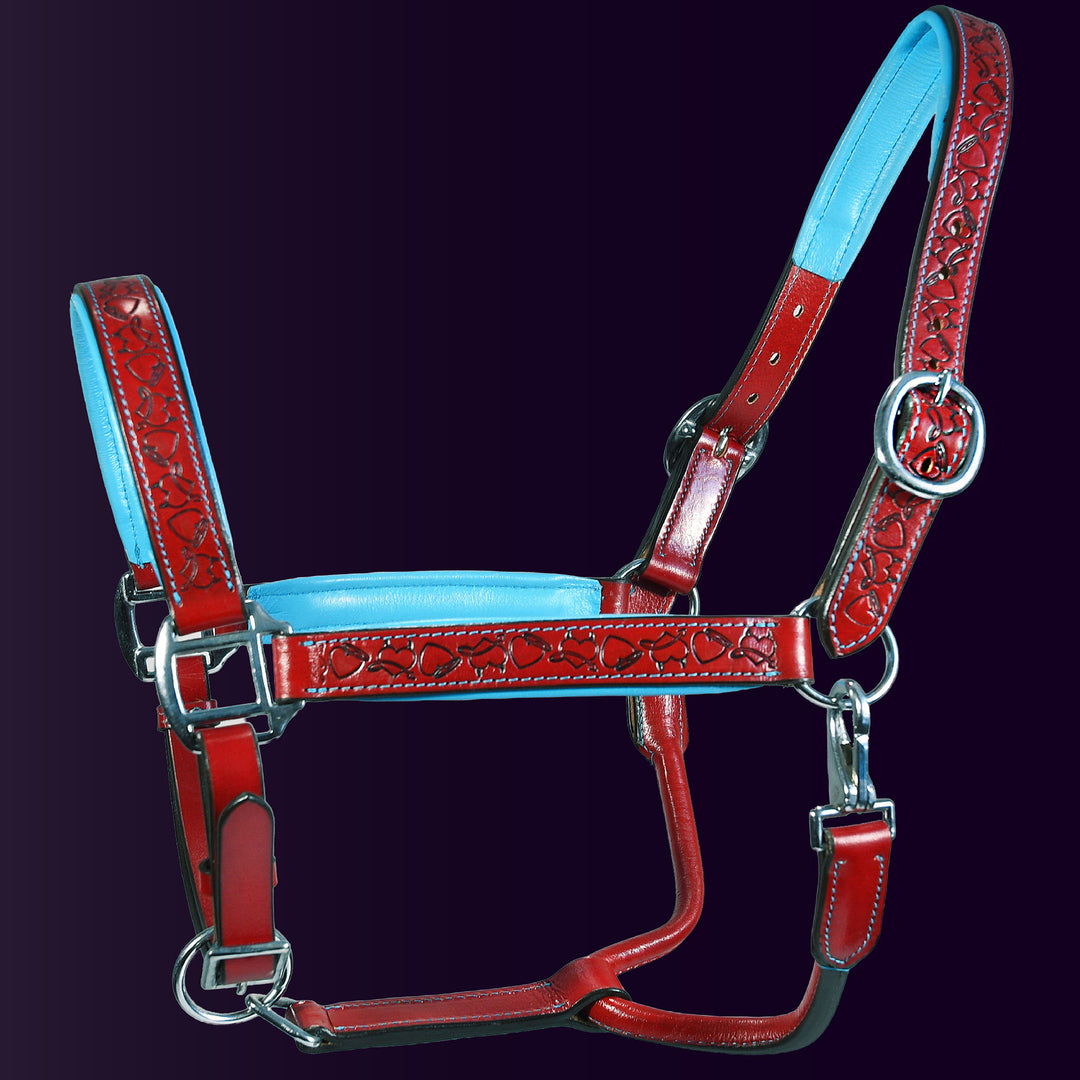 Full front view of the Wiskadero Halo and Horns padded leather halter. Highlights the red leather with deeply tooled halo, horn, and heart motifs, vibrant light blue padded leather lining at the crown, noseband, and cheeks, and polished chrome hardware against a dark purple background.