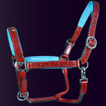 Full front view of the Wiskadero Halo and Horns padded leather halter. Highlights the red leather with deeply tooled halo, horn, and heart motifs, vibrant light blue padded leather lining at the crown, noseband, and cheeks, and polished chrome hardware against a dark purple background.