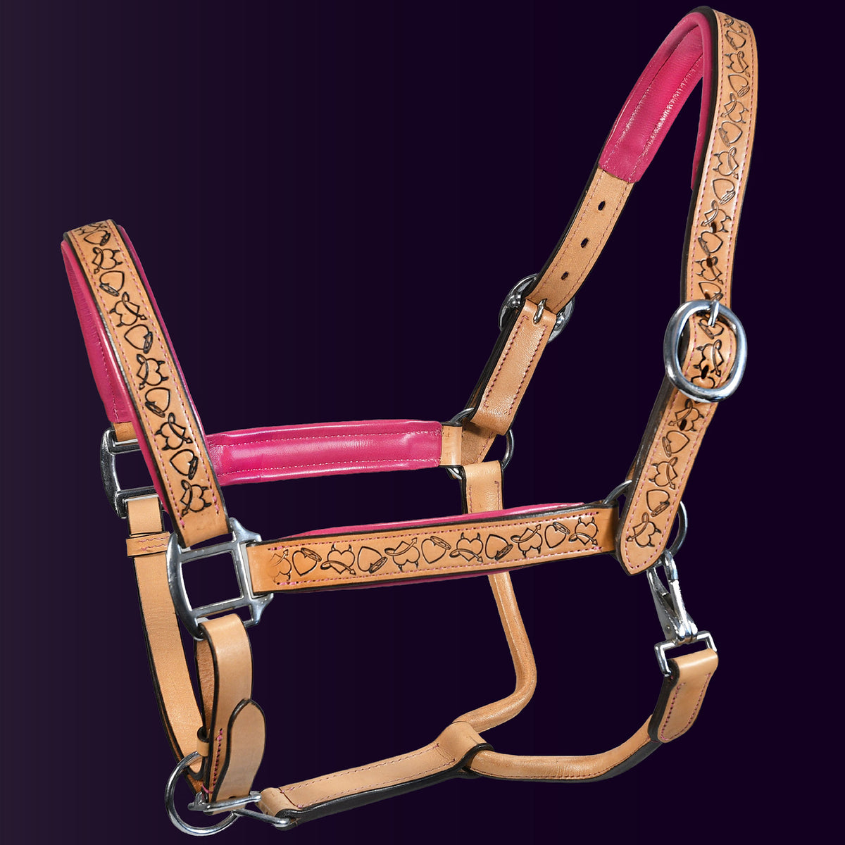 Full view of the Wiskadero Halo and Horns padded leather halter. Highlights the tan saddle leather with deeply tooled halo, horn, and heart motifs, vibrant raspberry/pink padded leather lining at the crown, noseband, and cheeks, and polished chrome hardware.