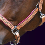 Close-up detail view of the left side of a bay horse wearing the Wiskadero Halo and Horns padded halter, showing the deeply tooled halo, horn, and heart motifs on tan saddle leather, vibrant raspberry/pink padded lining, and polished chrome hardware against a dark purple background.