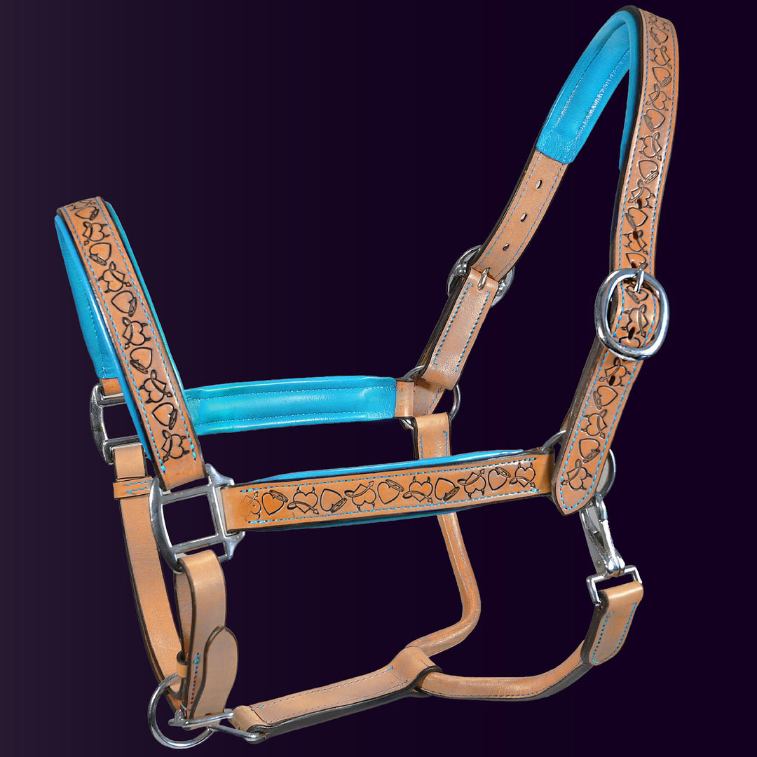 Full front view of the Wiskadero Halo and Horns padded leather halter. Highlights the tan saddle leather with deeply tooled halo, horn, and heart motifs, vibrant turquoise blue padded leather lining at the crown, noseband, and cheeks, and polished chrome hardware against a dark purple background.