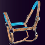 Full front view of the Wiskadero Halo and Horns padded leather halter. Highlights the tan saddle leather with deeply tooled halo, horn, and heart motifs, vibrant turquoise blue padded leather lining at the crown, noseband, and cheeks, and polished chrome hardware against a dark purple background.